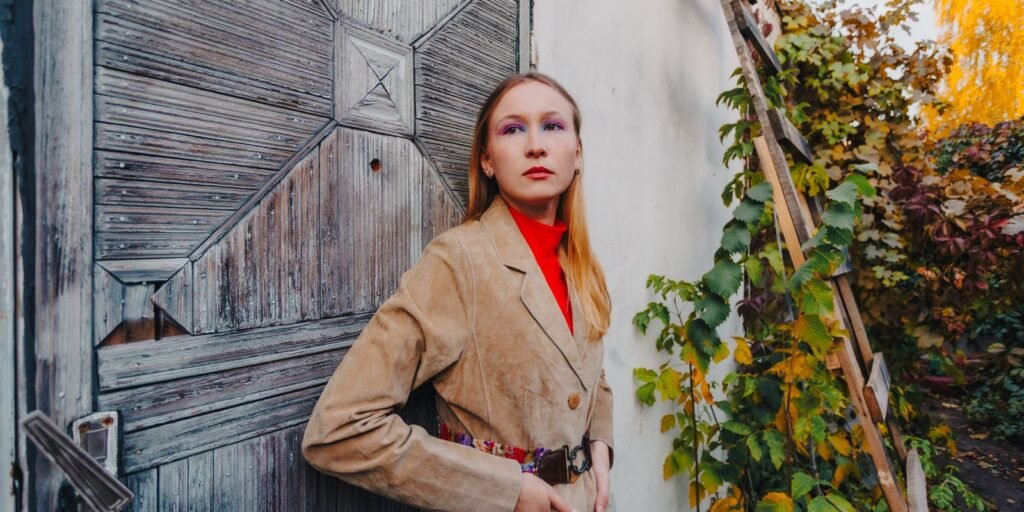 Donna con giacca di camoscio color cuoio appoggiata a una vecchia porta logorata nella luce d autunno