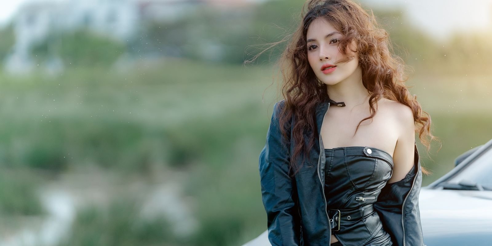 Giovane donna con giubbotto di pelle in posa sicura all'aperto vicino a un'auto
