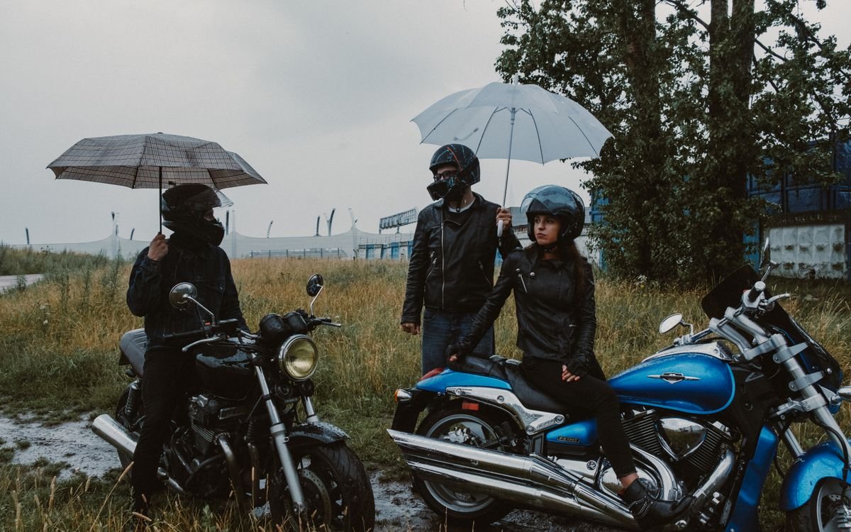 Motociclisti al riparo dalla pioggia sotto ombrelli in un campo erboso