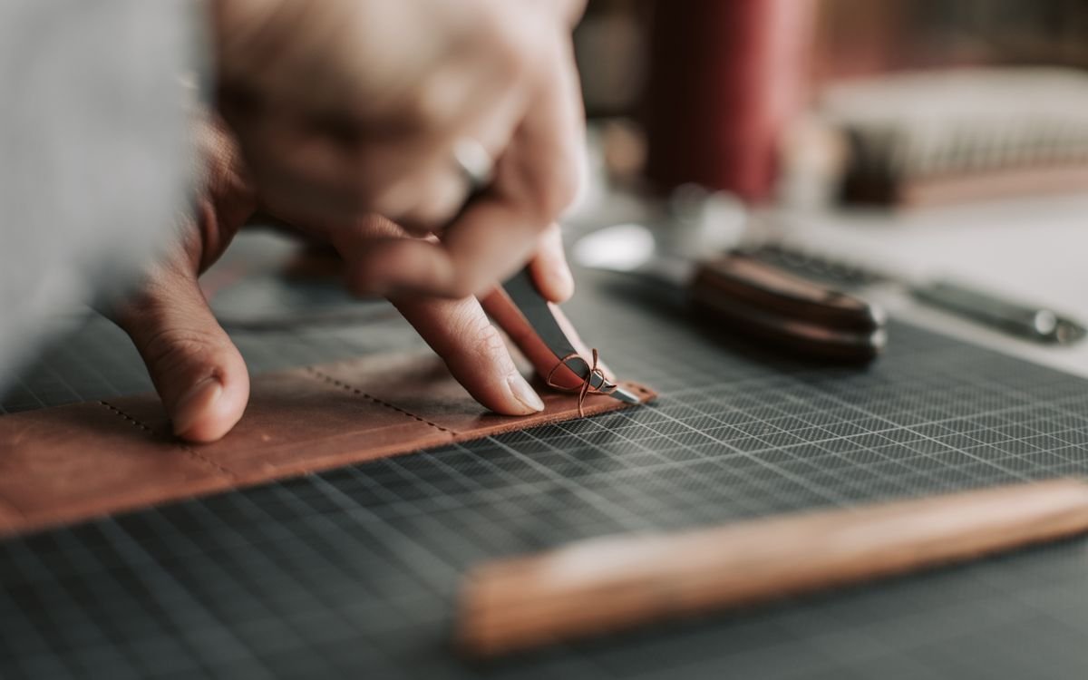 Primo piano di mani che lavorano con cura un pezzo di pelle in un laboratorio