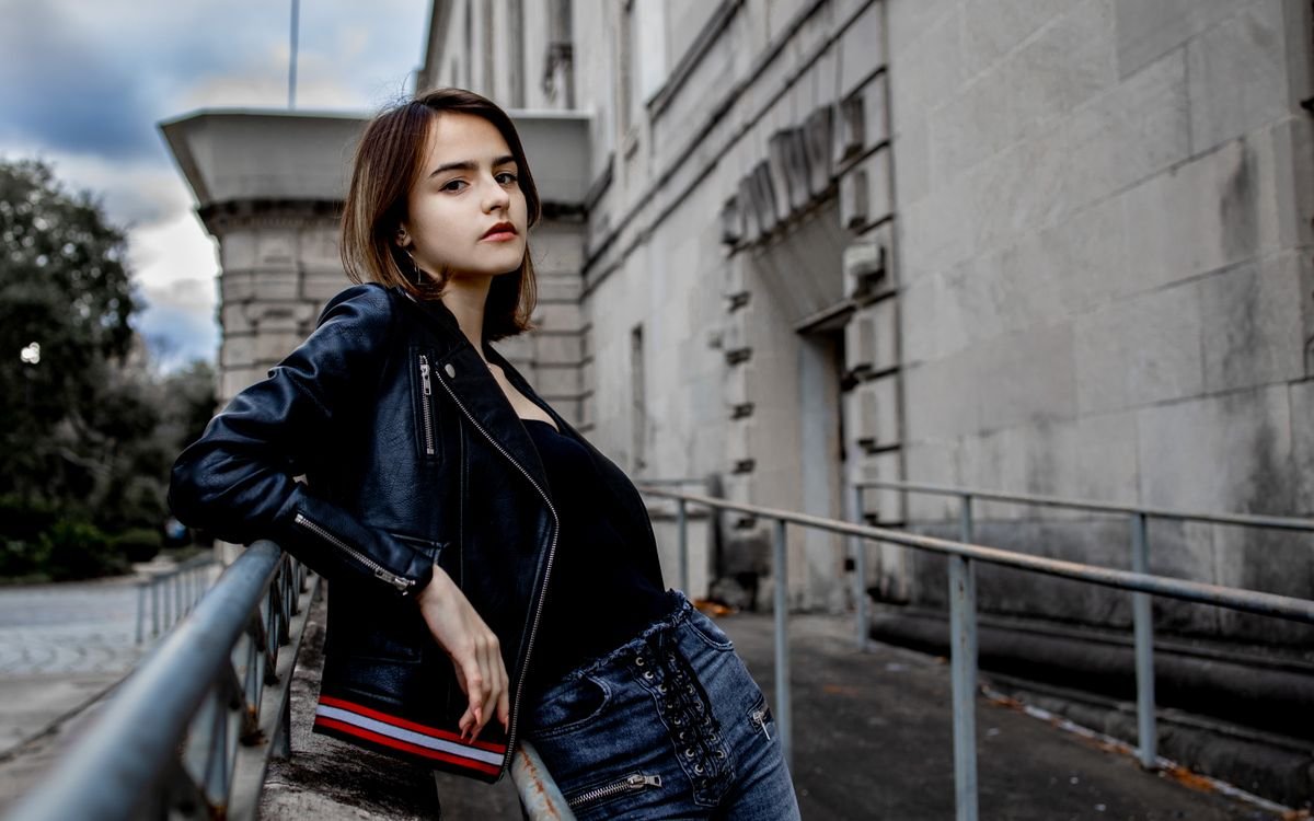 Giovane donna alla moda in posa sicura con una giacca di pelle su uno sfondo urbano