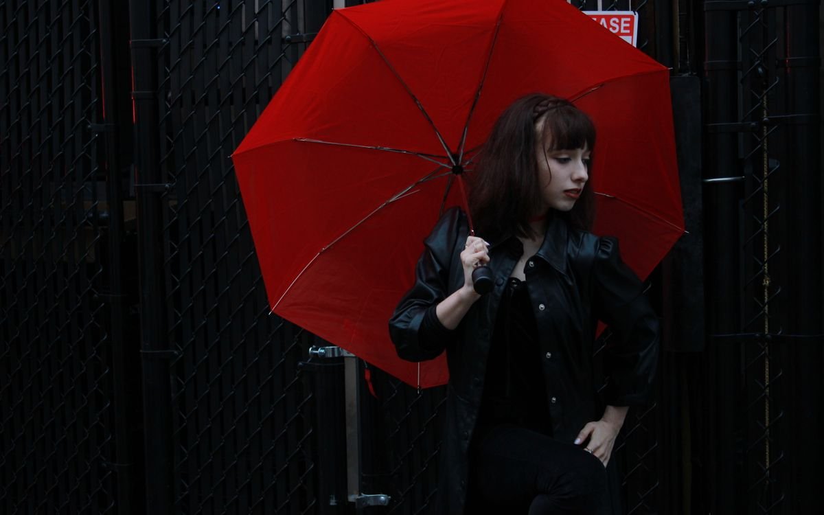 Donna con giacca di pelle nera e ombrello rosso all'aperto