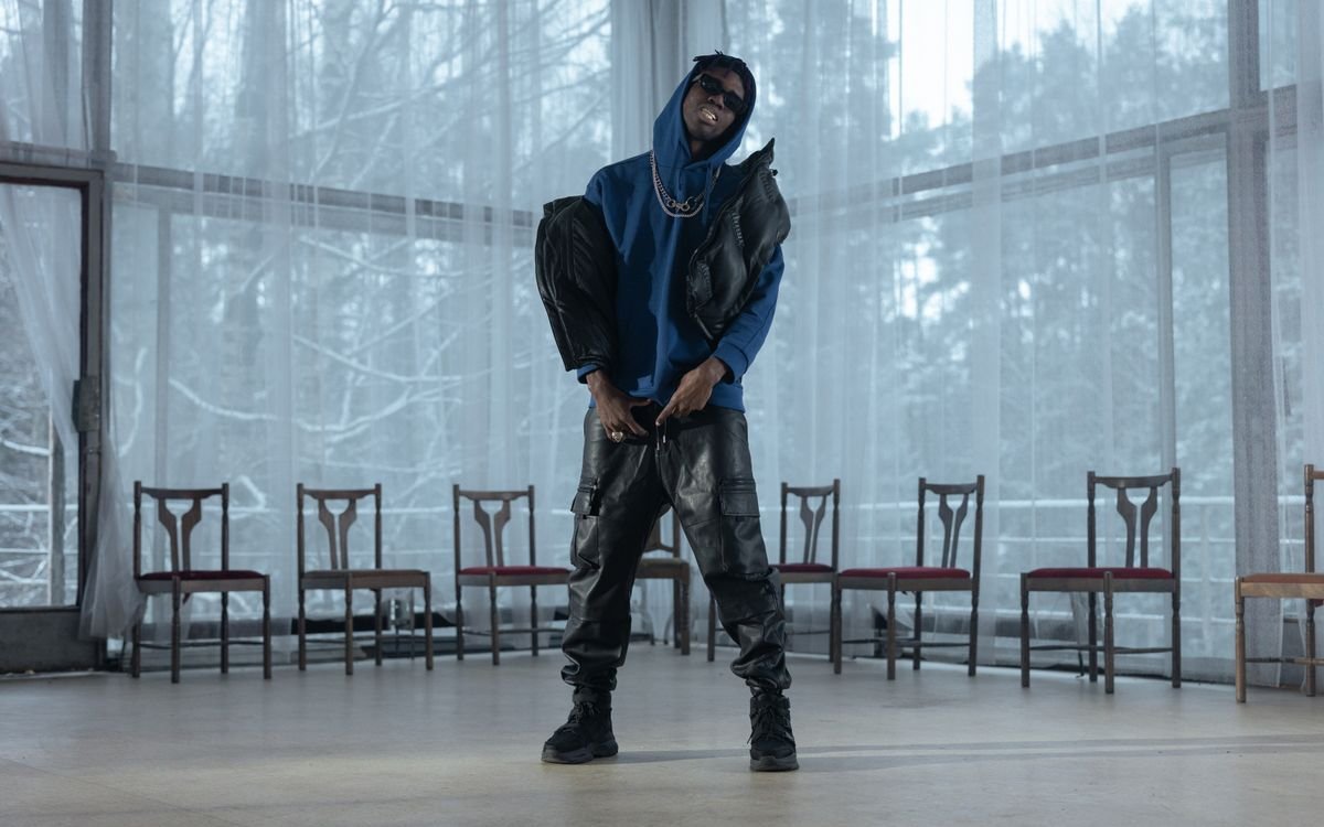 Uomo elegante con felpa blu e pantaloni di pelle in posa d'interni con illuminazione drammatica
