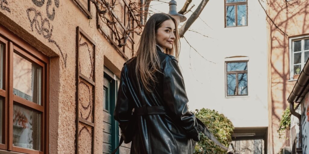Donna elegante in un lungo cappotto di pelle nera che cammina in una strada piena di graffiti