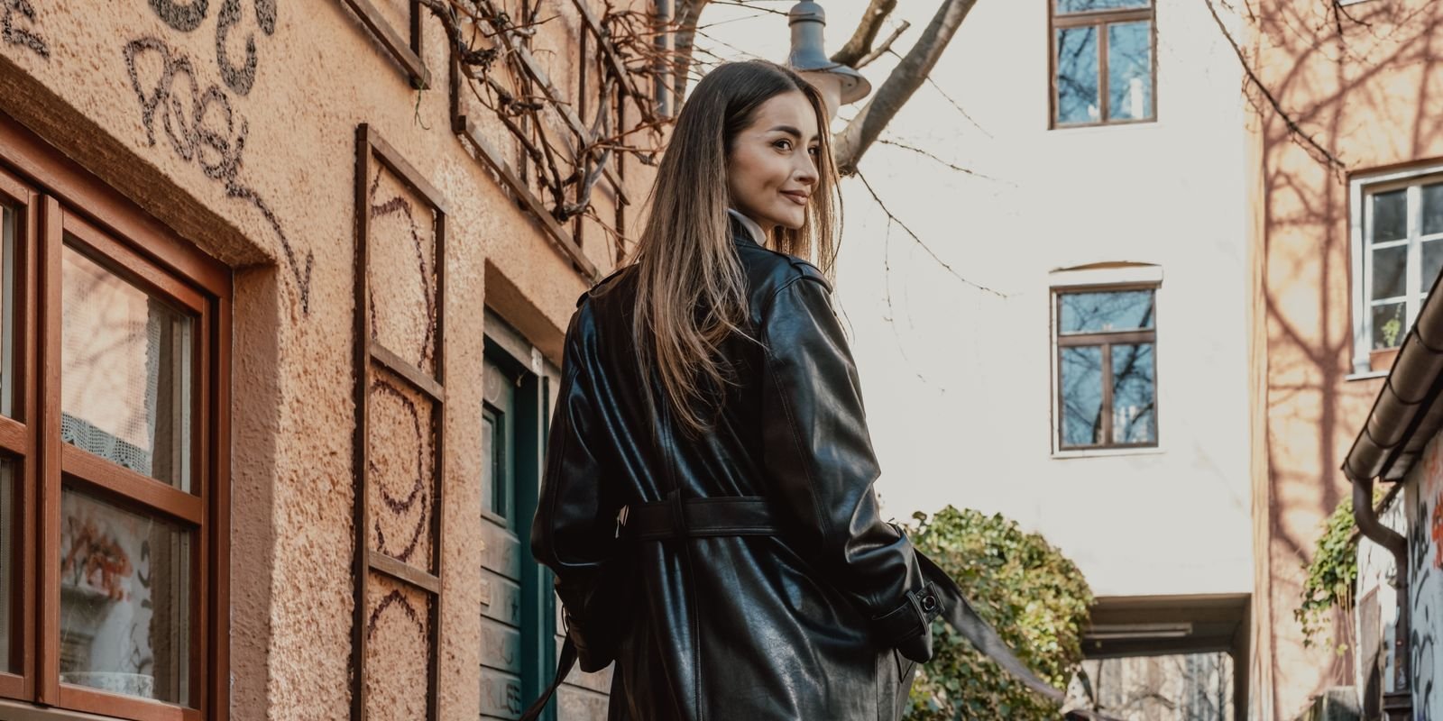 Donna elegante in un lungo cappotto di pelle nera che cammina in una strada piena di graffiti