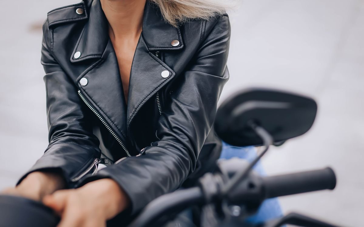 Primo piano di una donna con giacca di pelle nera dal collo alto in sella a una moto