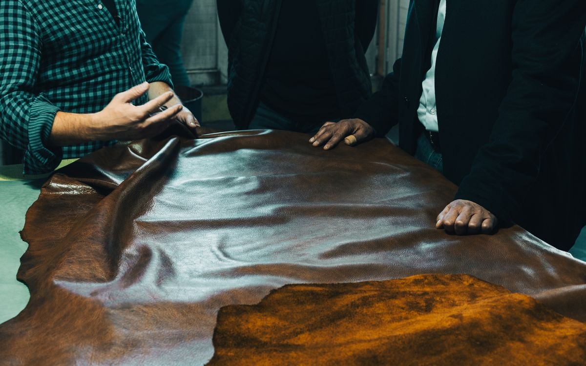 Gruppo di artigiani che esamina la pelle su un tavolo, concentrati sulla qualità e sulla scelta del materiale