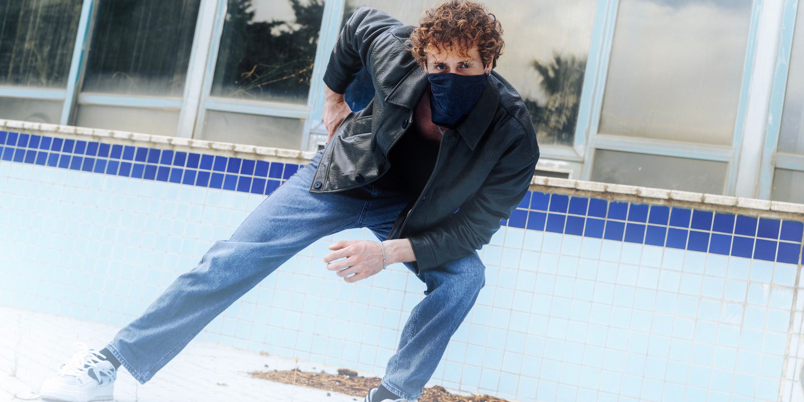Uomo con giacca di pelle e jeans appoggiato a un muro in una posa elegante e rilassata