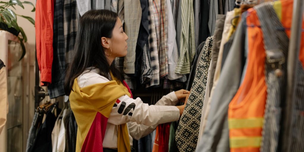 Una giovane donna sfoglia una rastrelliera di abiti in un negozio vintage pieno di capi colorati