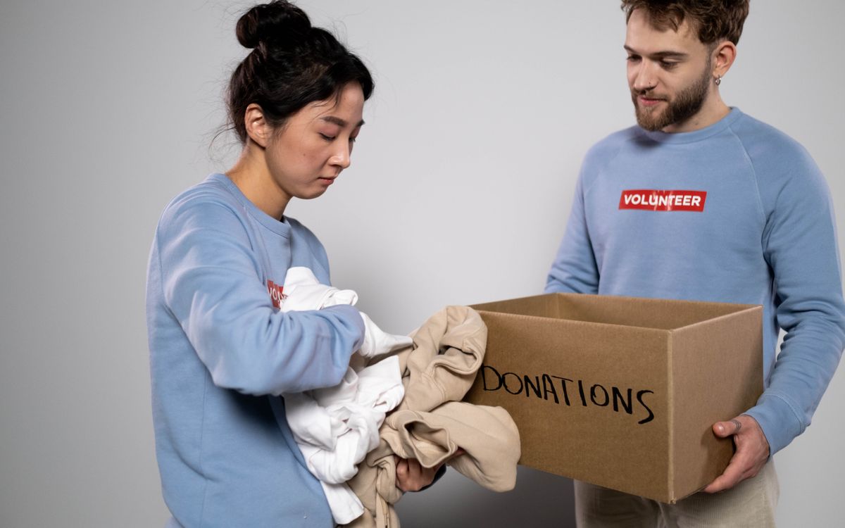 Due volontari sistemano gli abiti in una scatola per le donazioni, mostrando servizio alla comunità e generosità