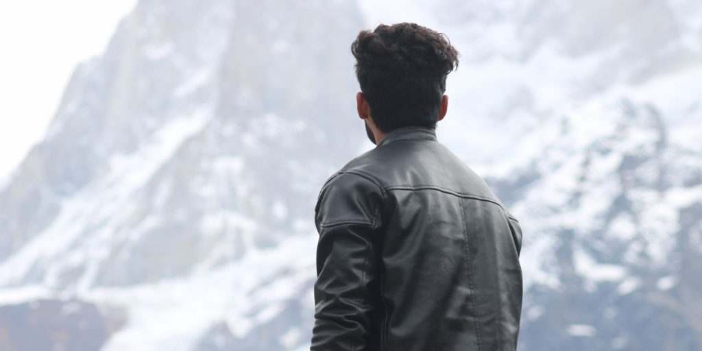 Un uomo con una giacca di pelle guarda montagne innevate sotto un cielo invernale limpido