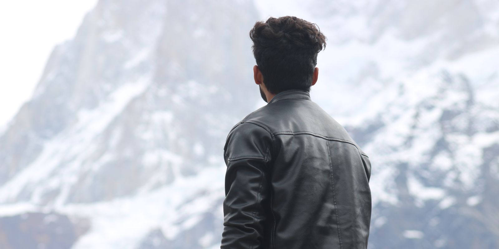 Un uomo con una giacca di pelle guarda montagne innevate sotto un cielo invernale limpido