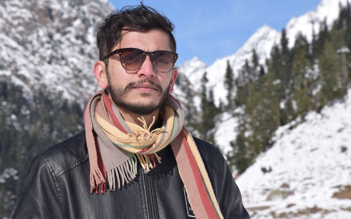 Un uomo con una sciarpa davanti a montagne innevate in una giornata fredda e limpida