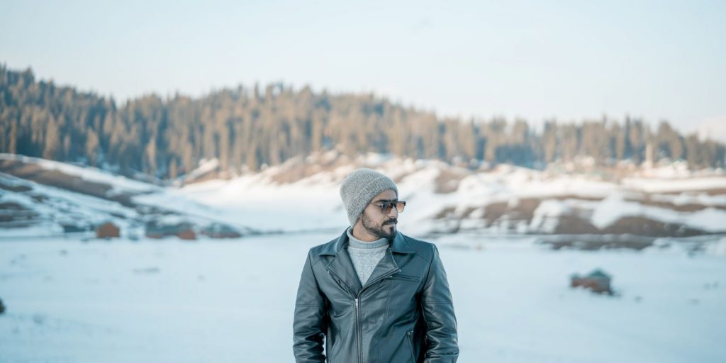 Un uomo in giacca di pelle tra montagne innevate sotto un cielo limpido