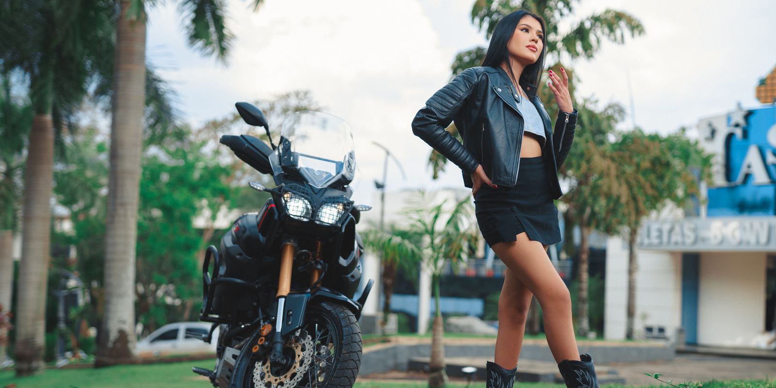 Donna sicura di sé con una giacca biker di pelle accanto a una moto al sole