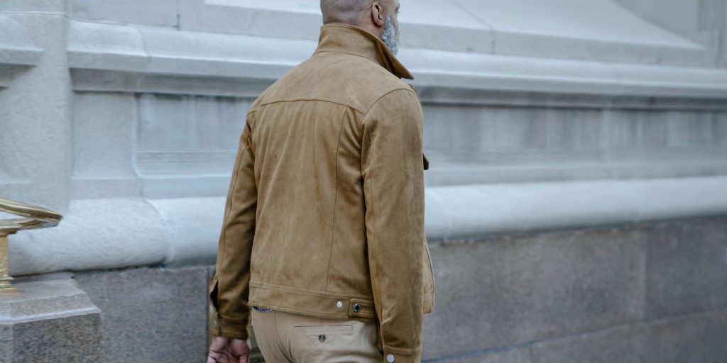 Uomo con un'elegante giacca di pelle marrone cammina accanto a un edificio classico