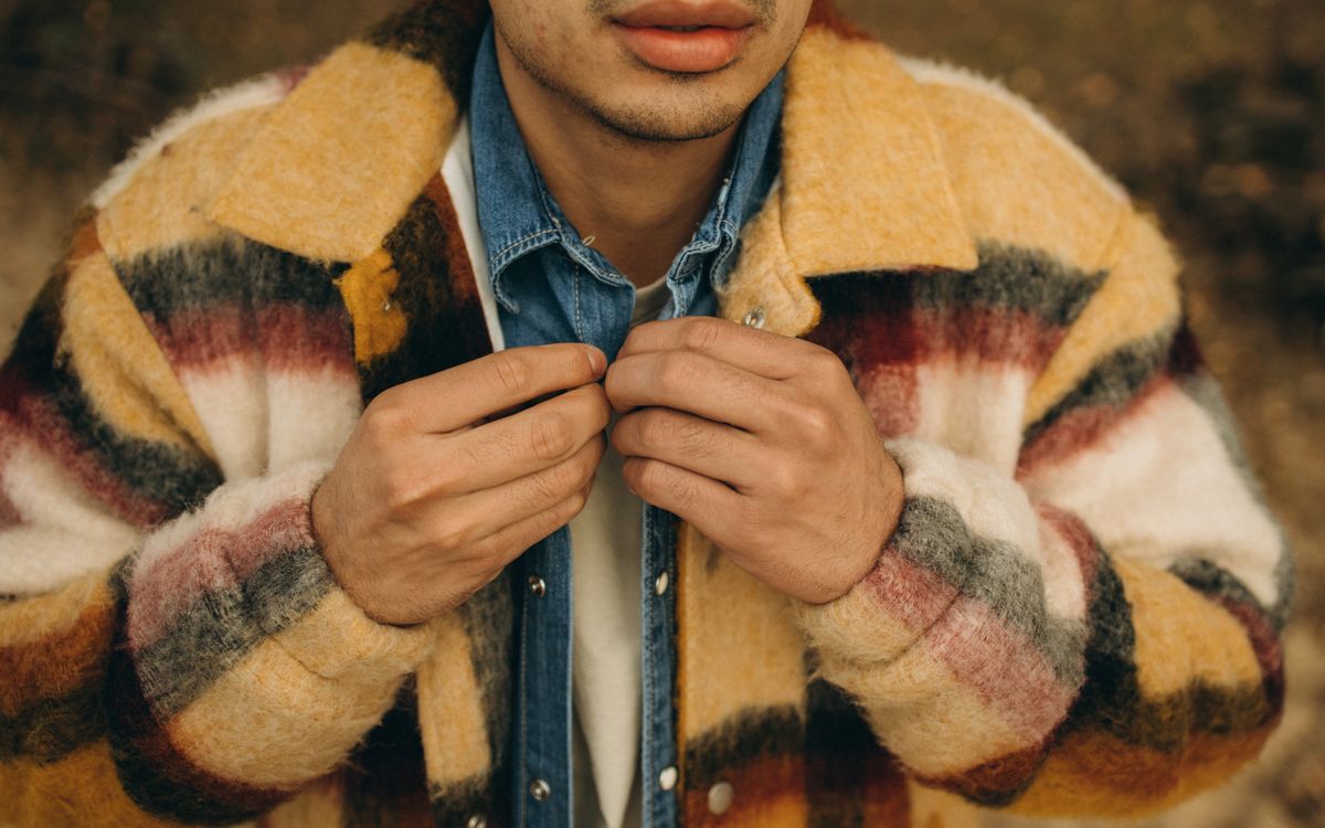 Un uomo sistema il collo del suo overshirt all'aperto in una fresca giornata d'autunno