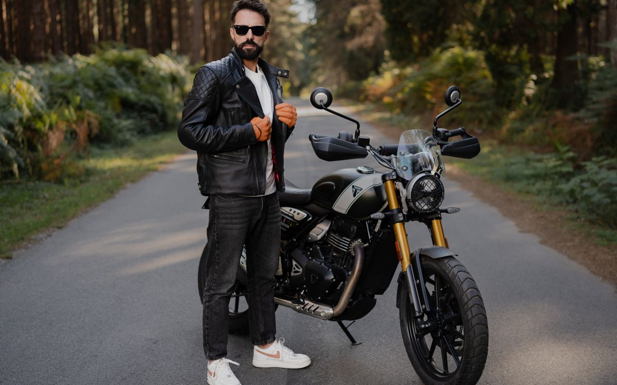 Un uomo elegante posa con una moto su una strada aperta