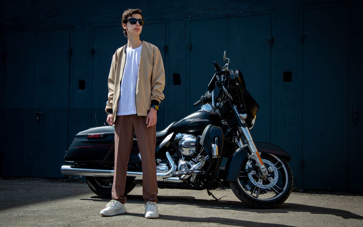 Un uomo in stile casual in posa con una motocicletta all'aperto