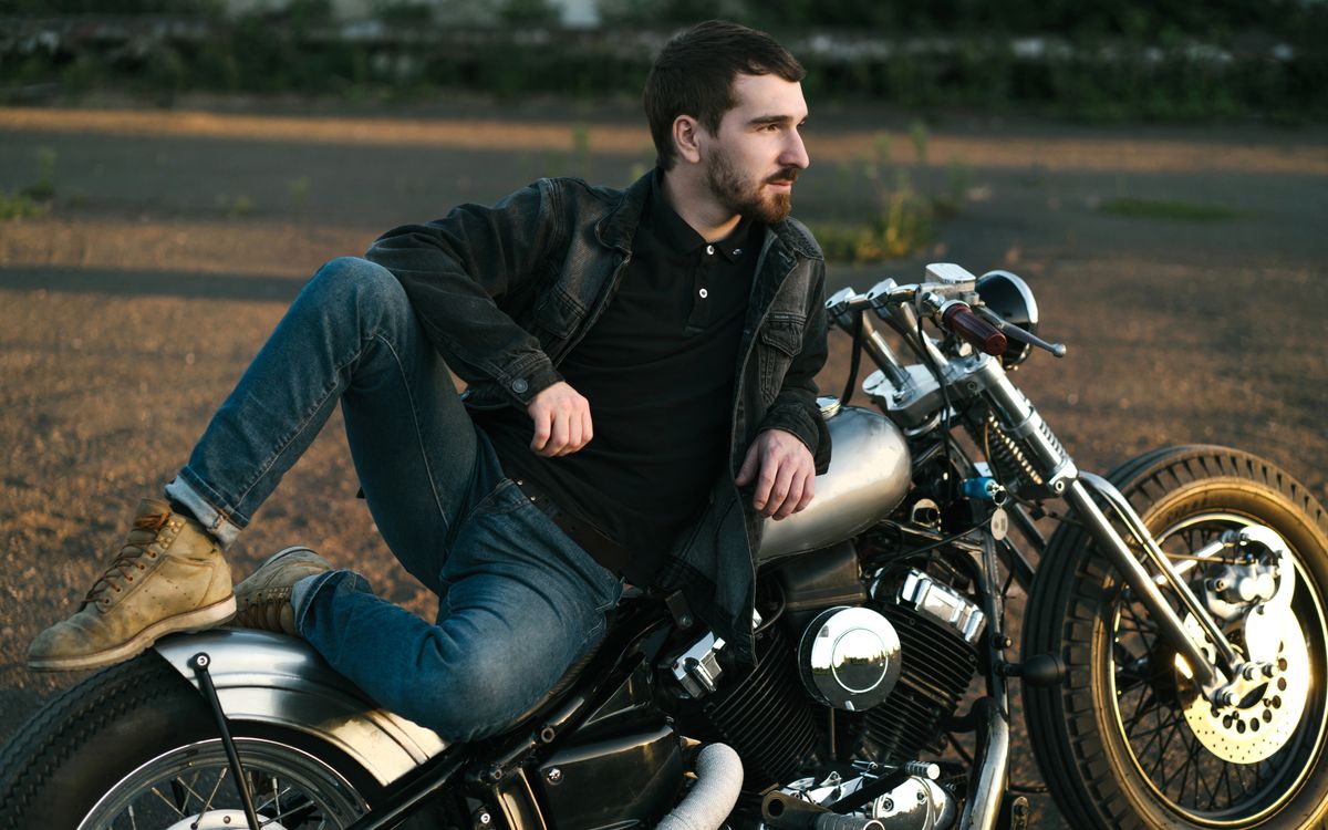 Giovane uomo con la barba rilassato accanto a una moto personalizzata
